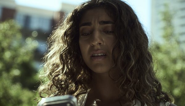 The Actor outdoors in daylight, looking down at her phone as her face falls.
