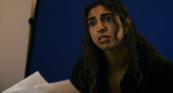 The Actor holding her script pages against a lit backdrop, mid-take.