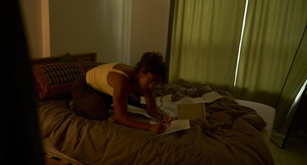 The Actor kneeling on her bed at night, marking up script pages across the duvet.