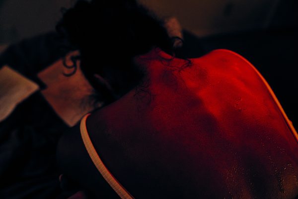 The Actor face down, her bare back and shoulders washed in hard red light.