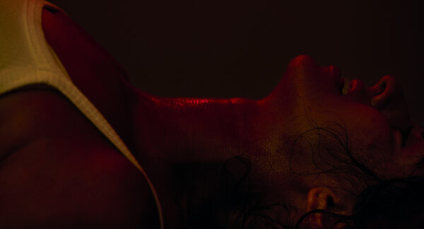 The Actor lying back under hard red light, throat exposed.